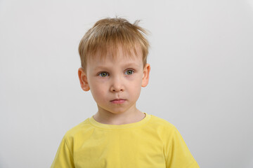 Fototapeta premium portrait of a little boy in a yellow t-shirt on a white background. the boy shows sadness
