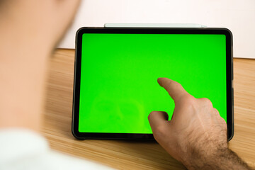 Man uses a tablet with chromakey for the work. Mobile phone on the wireless charger on the background. 