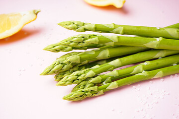 Fresh green asparagus and lemon wedges on pink background, close-up.