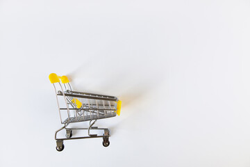 Small empty decorative shopping cart toy with yellow accents on a white background, place for text....