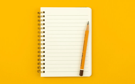 Notepad With Pencil On A Bright Colorful Orange Table And Background, Top View Photo With Copy Space