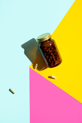 Vitamin magnesium capsules. pills in glass bottle on yellow, pink,blue background with trendy shadows. Concept wellness, mental health lifestyle.Modern creative minimalistic photo.Bold color.Vertical - obrazy, fototapety, plakaty