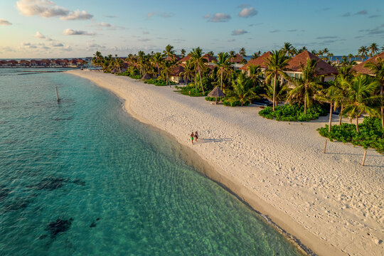 Aerial view of a couple walking on the beach on a paradise island at sunset near a luxury resort on Alifu Dhaalu Atoll, Alif Alif, Maldives.
