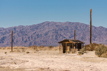 USA, CA, Salton Sea - December 28, 2012: Wooden brown shack lost in dunes of beige sand with...