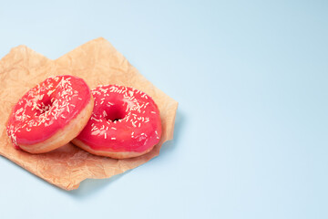 Pink fried donuts on crumpled parchment on a light blue background.