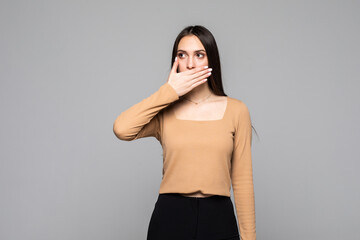 Pretty young woman covering her mouth over grey background