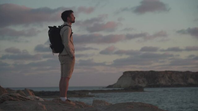 Male tourist with backpack watching beautiful view of Yeronisos Holy Island near coast Agios Georgios Pegeias In Cyprus. Man hiker looks into distance at deserted island in mediterranean sea