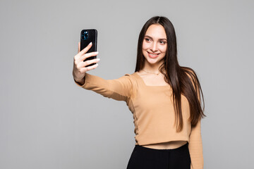 Naklejka premium Smiling young woman making selfie photo on smartphone over gray background