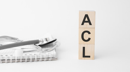 acl inscription on wooden cubes isolated on white background, medicine concept. Nearby on the table are a stethoscope and pills.
