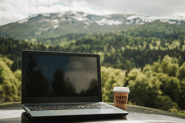 outdoors working on laptop, with coffee cup, remote location in nature with beautiful mountains...