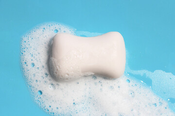 Soap bar in foam on blue background.