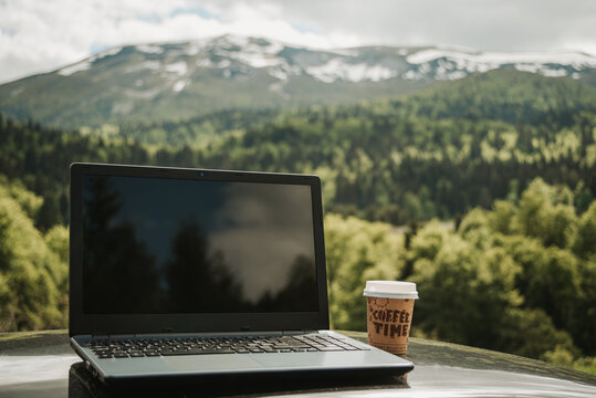 outdoors working on laptop, with coffee cup, remote location in nature with beautiful mountains internet connection