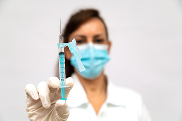Seringa de vacina em foco nas mãos de uma médica com luvas e mascara cirugica desfocado ao fundo