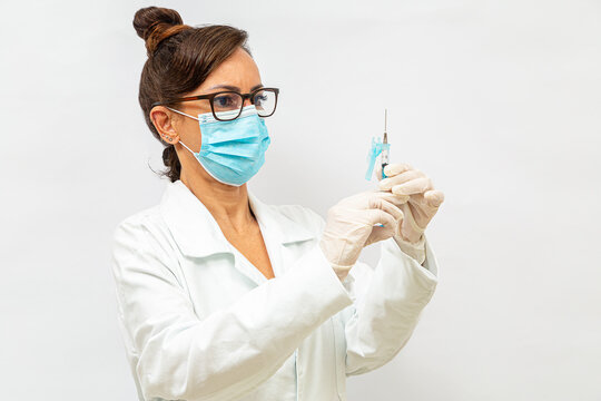 M&eacute;dica de &oacute;culos, usando m&aacute;scara protetora, segurando uma seringa com as duas m&atilde;os usando luvas cir&uacute;rgicas.