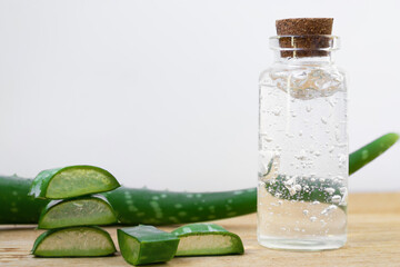 Glass bottle of aloe vera gel with whole leaves and plant pieces on wooden background