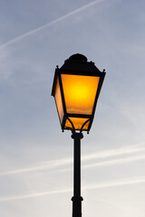 Lit antique street lamp against a cloudy sky