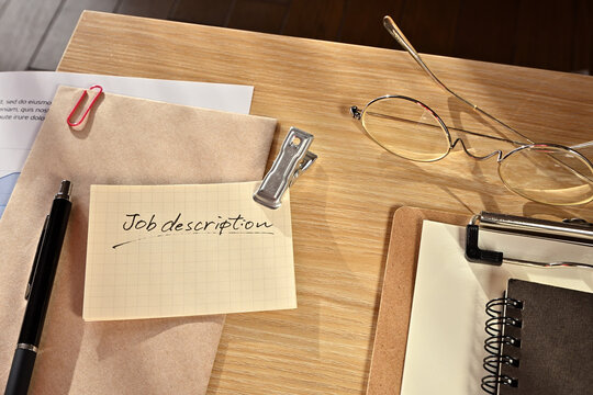 There is a piece of paper with the word of Job discription on the desk with a clipboard, a pen and glasses.