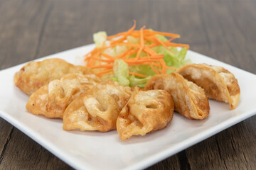 Deep fried gyoza arranged in an arc on a plate with garnishments for presentation