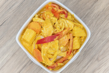 Overhead view of spicy yellow curry presented perfectly in a bowl served upon a wooden plank table