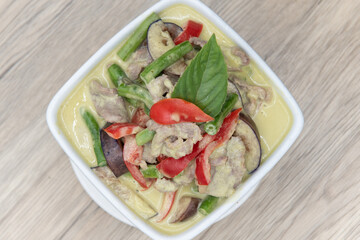 Overhead view of spicy green curry presented perfectly in a bowl served upon a wooden plank table