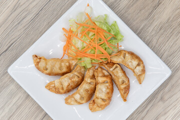 Overhead view of deep fried gyoza arranged in an arc on a plate with garnishments for presentation