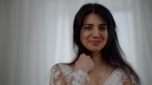Close-up portrait of happy smiling young Middle Eastern woman in white beautiful wedding dress posing indoors. Gorgeous confident bride looking at camera rejoicing on wedding morning