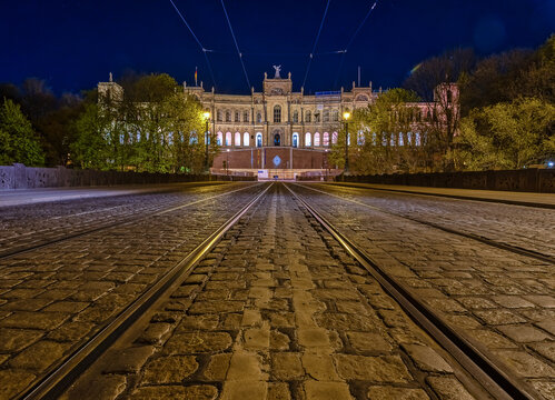 Low perspective symmetrical view over a tram track with popular Munich architecture in the background at night.
