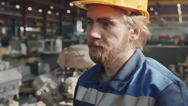 Tilt-up close-up with slowmo of bearded Caucasian factory worker in blue coverall uniform putting on yellow hard hat and safety glasses preparing for shift