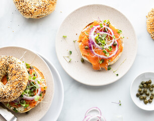 Top down view of a bagel topped with salmon lox and garnished with red onion, sprouts and capers.