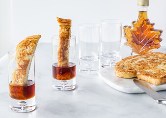 Two french toast shot glass appetizers with empty shot glasses, french toast and maple syrup to prepare more of the same
