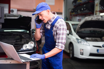 Confident auto mechanic talking on a smartphone in a car service