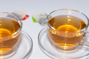 Two cups of black leaf tea with tea bags kept alongside with white background 