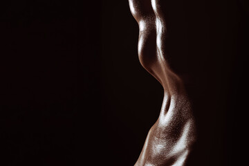 Fototapeta na wymiar Slender waist of a naked girl. Silhouette of wet tummy in drops of sweat on a dark background