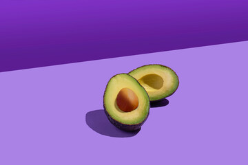 An avocado cut in half, both parts shown. Pop style. Background of violet colors of different shades. Copy space