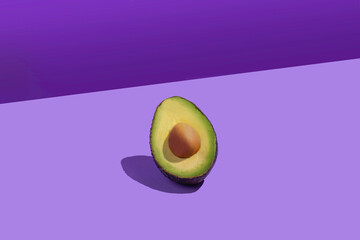 Half an avocado with stone. Pop style. Background of violet colors of different shades.