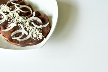 Overhead shot of traditional enfrijoladas with onion and cheese on white plate, white background, with copy space