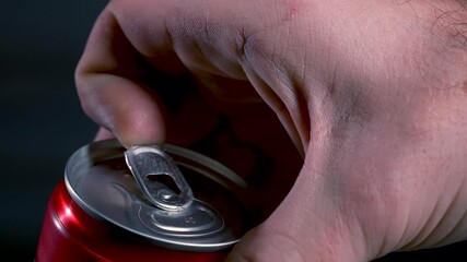 An adult opens a cold aluminum red can of a carbonated drink, beer on a black background. Close up of male fingers opening a beer can. Slow motion. - Powered by Adobe