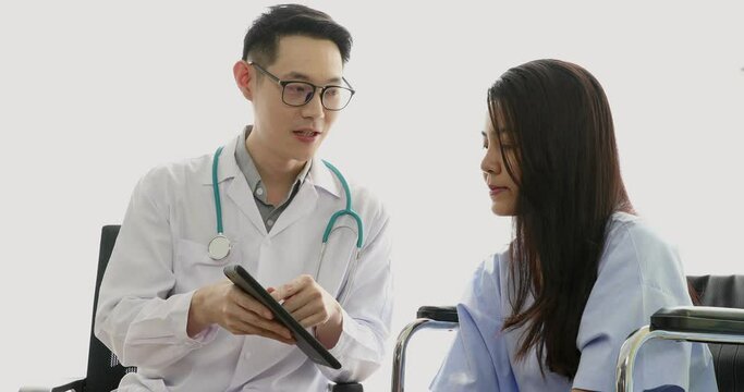Young nice asian doctor with glasses talking and giving his patient some recommendation on the health result by pointing and explaining using his tablet