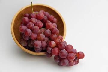 Fresh and ripe red grapes in a wooden bowl, isolated in white background. Bunch of raw and juicy grapevines