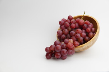 Fresh and ripe red grapes in a wooden bowl, isolated in white background. Bunch of raw and juicy grapevines