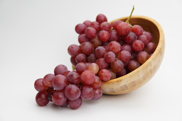 Fresh and ripe red grapes in a wooden bowl, isolated in white background. Bunch of raw and juicy grapevines