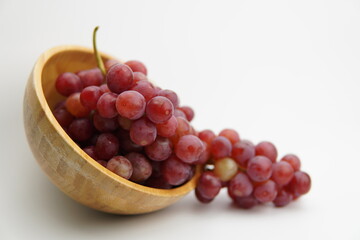 Fresh and ripe red grapes in a wooden bowl, isolated in white background. Bunch of raw and juicy grapevines