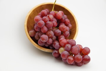 Fresh and ripe red grapes in a wooden bowl, isolated in white background. Bunch of raw and juicy grapevines