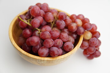Fresh and ripe red grapes in a wooden bowl, isolated in white background. Bunch of raw and juicy grapevines