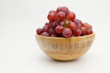 Fresh and ripe red grapes in a wooden bowl, isolated in white background. Bunch of raw and juicy grapevines