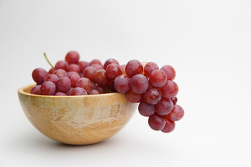 Fresh and ripe red grapes in a wooden bowl, isolated in white background. Bunch of raw and juicy grapevines