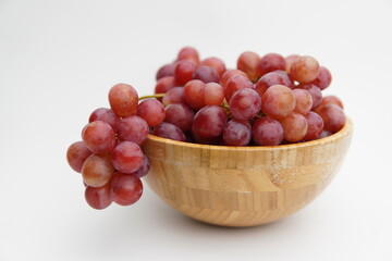 Fresh and ripe red grapes in a wooden bowl, isolated in white background. Bunch of raw and juicy grapevines