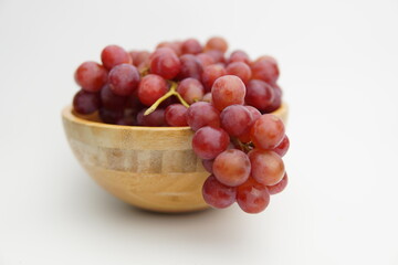 Fresh and ripe red grapes in a wooden bowl, isolated in white background. Bunch of raw and juicy grapevines