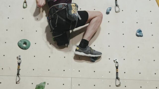 Rear-view slowmo of athletic man with amputated leg climbing wall indoors at sports complex wearing safety equipment. Concept of strength and motivation