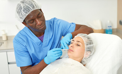 Obraz na płótnie Canvas Dermatologist male preparing woman client before aesthetic facial procedure in medical office